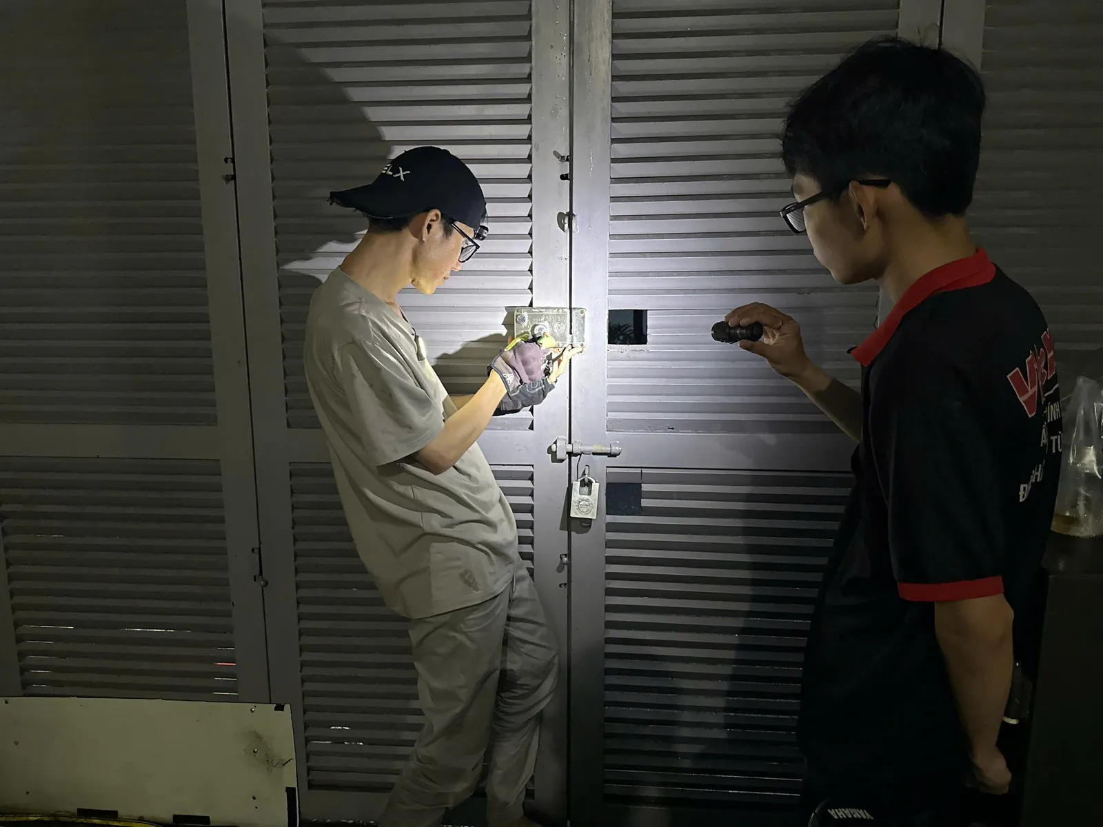 Hai thợ soi đèn mở khóa cửa sắt lá sách ban đêm