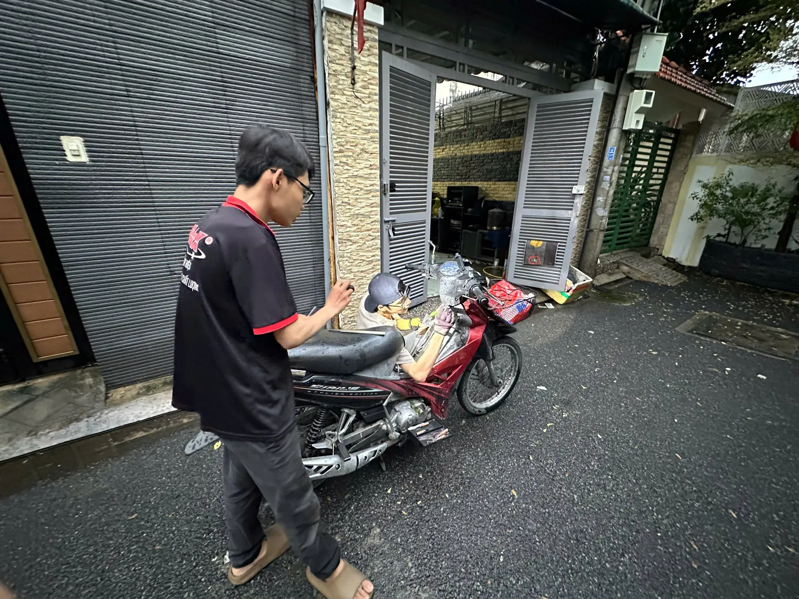 Thợ khóa đứng bên xe màu đỏ, thợ khác ngồi xử lý ổ khóa