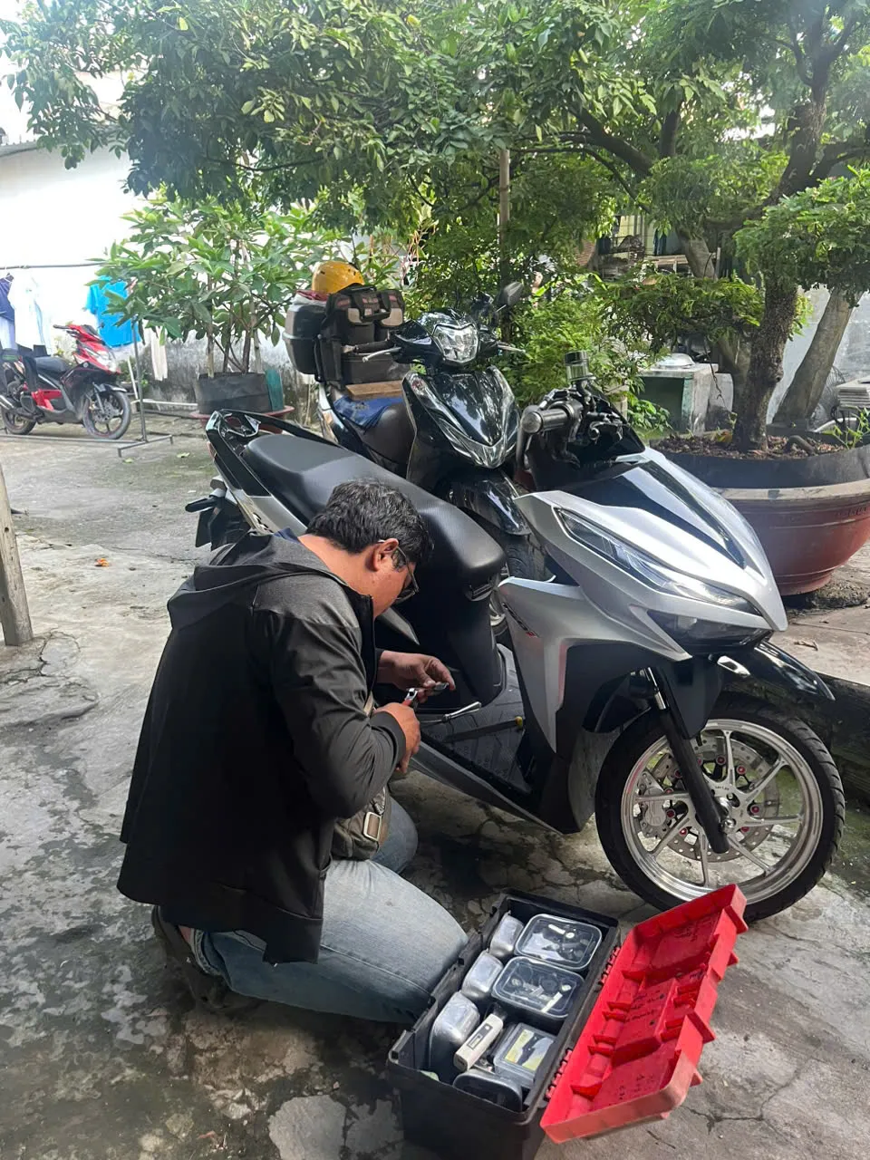 Thợ quỳ sửa khóa xe tay ga, hộp đồ nghề bên cạnh
