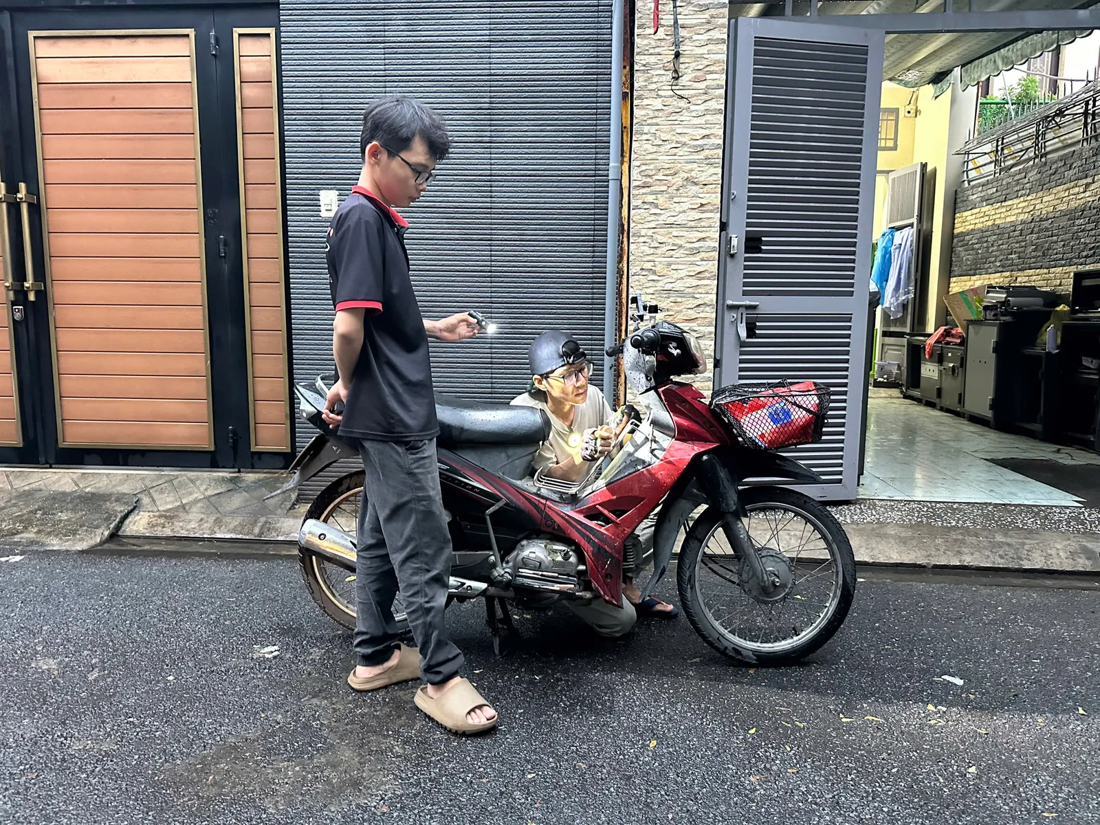 Thợ ngồi soi đèn xử lý ổ khóa xe máy màu đỏ trong hẻm